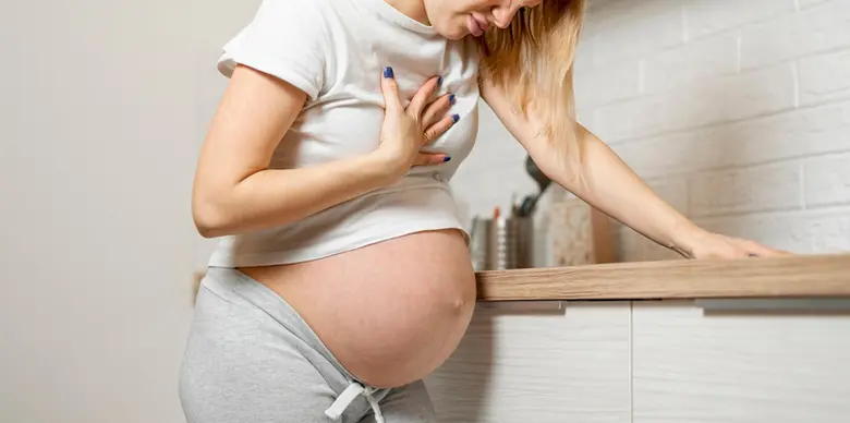 Těhotná žena drží ruku na břiše v kuchyni.