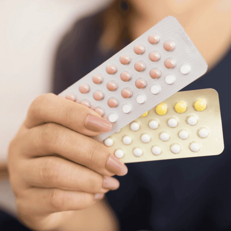 Žena drží v rukou balení hormonální antikoncepce s pilulkami.