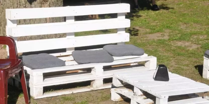 Bílá lavice z palet s polštáři venku na trávě