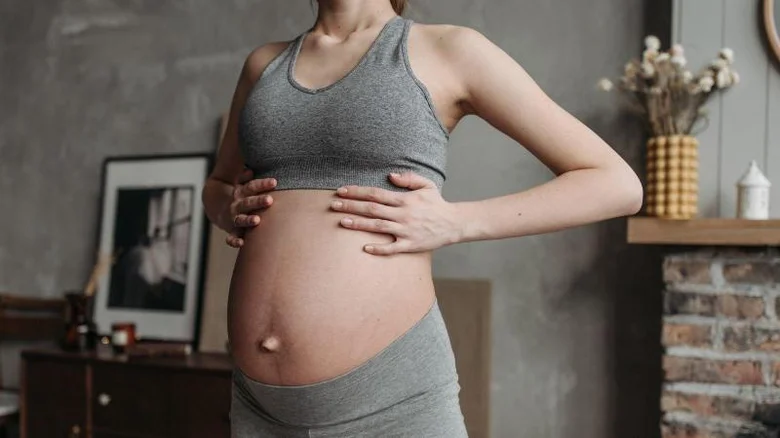 Těhotná žena drží ruce na svém břiše.