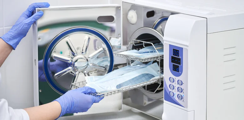 Person v modrých rukavicích vkládá do autoklávu při sterilizaci.