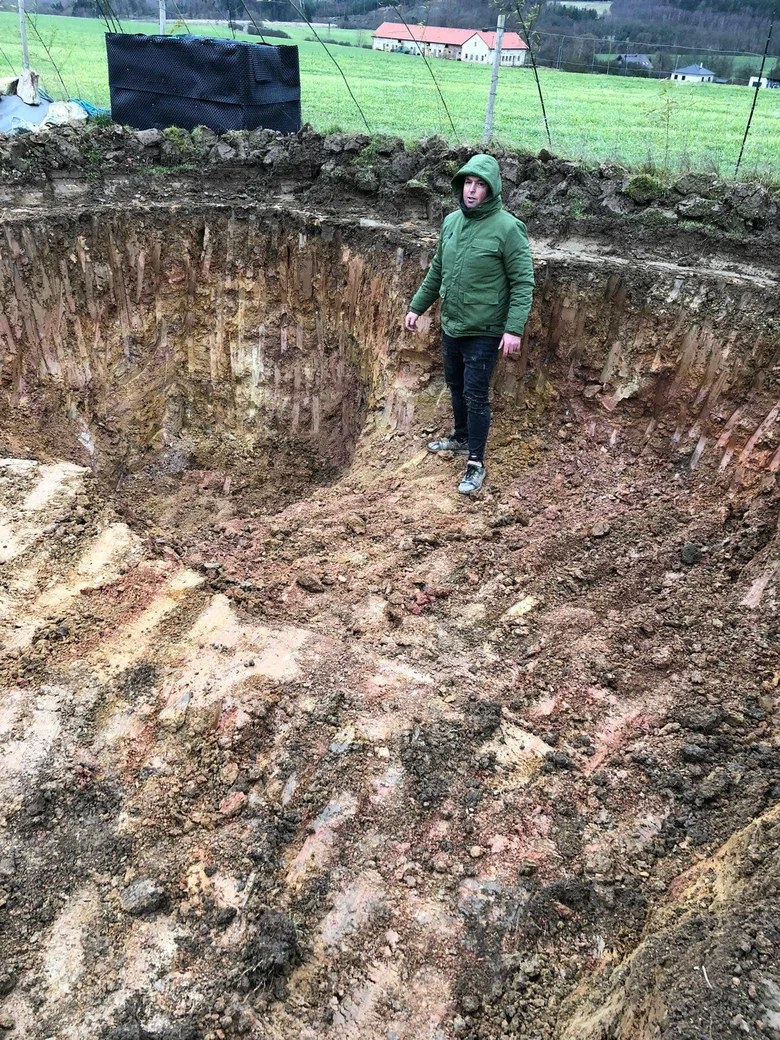 Muž stojí v vykopaném jámě pro budování zahradního koupacího biotopu.