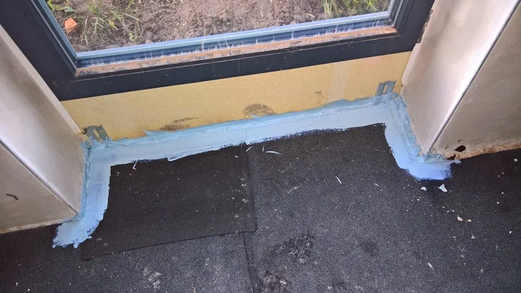 Modrá hydroizolační hmota je aplikována na základovou spáru okna.