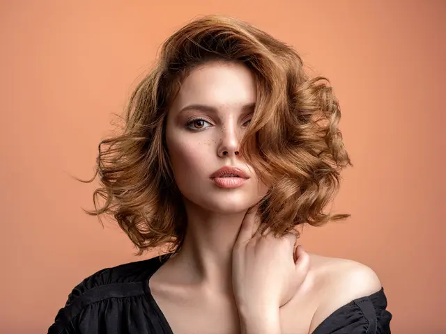 Žena s objemnými vlnitými vlasy dotýká se krku na oranžovém pozadí.