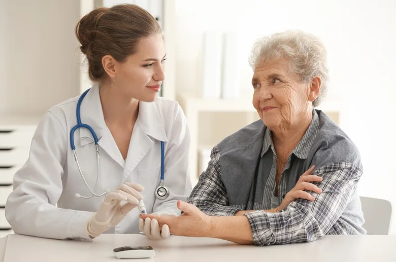 Lékařka měří hladinu cukru v krvi seniorce při kontrole příznaků cukrovky.