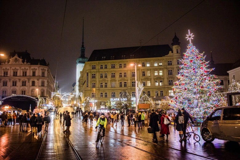 Vánoční trh na náměstí s ozdobeným stromem a lidmi v noci.