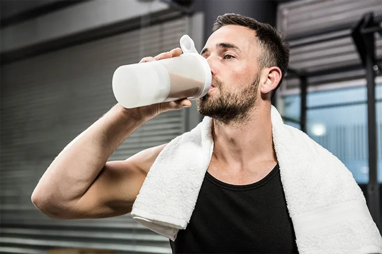 Muž pije proteinový nápoj po tréninku v posilovně.