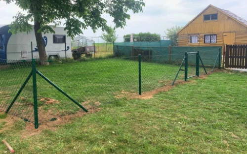 Zelená plotová síť se montuje na trávníku vedle domu.