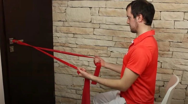 Muž cvičí s gumovou páskou pro rehabilitaci ramene.
