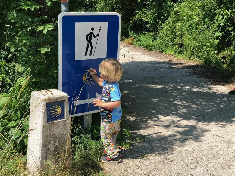 Dítě dotýká se modlé značky s křížem na stezce Camino de Santiago.