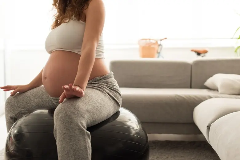 Těhotná žena sedí na cvičební kouli pro úlevu od bolesti zad.